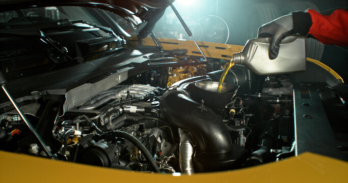 Mechanic pouring engine oil into car engine in workshop. Automotive maintenance, oil change service and professional repair concept with dramatic lighting.