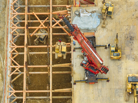 Aerial view of building foundation engineering with a large red crane and yellow excavators working on a steel framework at a construction site in Taiwan.