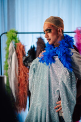 Naklejka premium Drag queen preparing for a performance, wearing makeup, a wig cap, and a blue boa, choosing a sparkling costume
