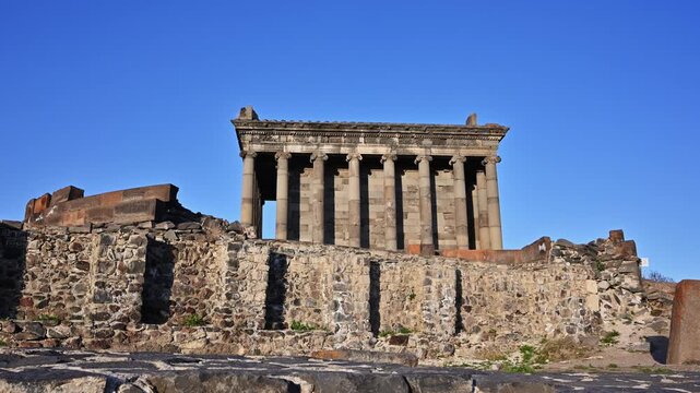 Ancient temple ruins under clear blue sky. Stone columns stand tall against bright daylight. Weathered walls surround the sacred structure