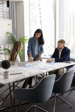 Group of professional marketing analysts reviewing campaign metrics and performance data, developing strategies or prepare report, gathered at conference table in contemporary boardroom with city view