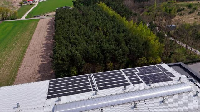 Aerial drone view of an industrial roof with photovoltaic solar panels, renewable energy installation, green technology, forest and farmland background, eco-friendly power, sustainability concept, cle