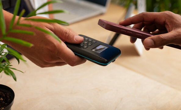 Mid-30s man and African non-binary person swapping devices on shop counter, phone tapping reader