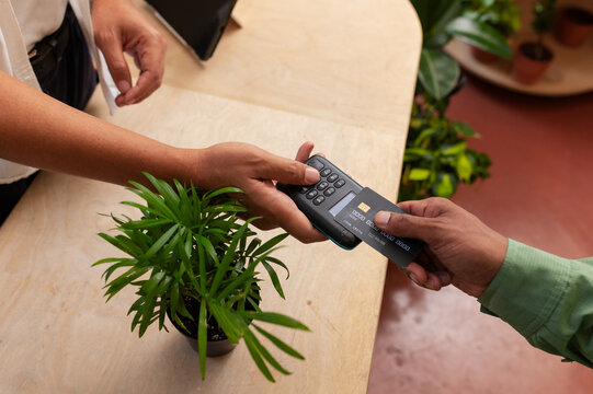 Vendor and customer exchanging payment at reader, tapping chip card, completing sale at plant shop