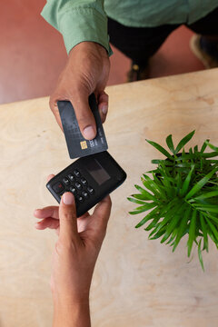 Customer and vendor exchanging payment at counter with chip card, black reader, plant, green sleeve