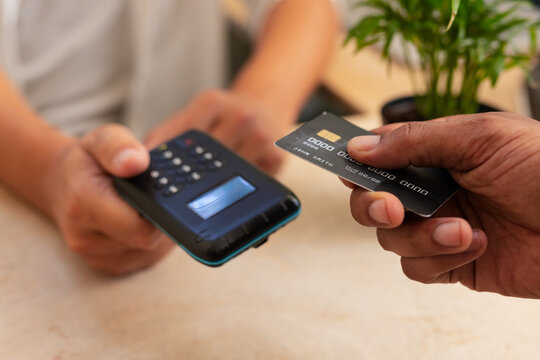 Clerk holding reader while African nonbinary buyer tapping black chip card to pay at counter