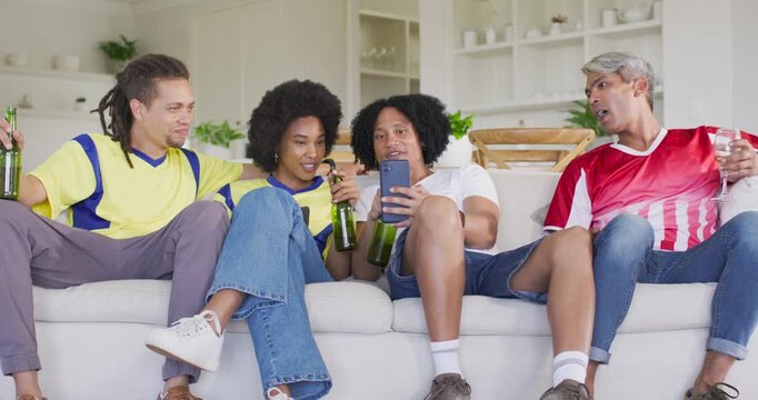 Diverse friends laughing as woman showing phone in living room with green bottles in jerseys