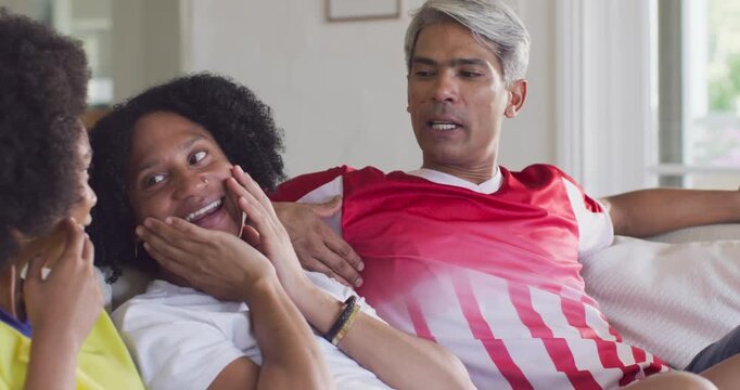 Diverse friends on couch in living room, mature man in red shirt sharing story, others laughing