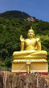 Aerial view of statue of a seated golden Buddha on a rock in a mountain temple. Aluvihara, Matale, Central Province, Sri Lanka. Vertical video.