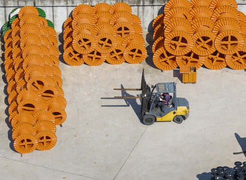 Aerial view of large orange cable reels stacked in an industrial yard with a yellow forklift and worker Taiwan.