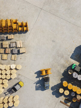 Aerial view of large industrial cable reels and wooden spools organized in a factory yard with a forklift moving equipment on concrete in Taiwan.