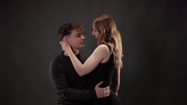 Passionate young man and woman in black clothes dancing together against a dark gray background