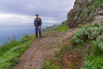 Obraz premium A hiker stands on a nature trail in Anaga Rural Park, with the ocean in the background. Tenerife. Canary Islands.
