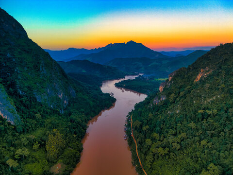 Aerial view of the winding Nam Ou River flowing through steep limestone karst mountains under a vibrant sunset sky Nong Khiaw, Luang Prabang Province, Laos.