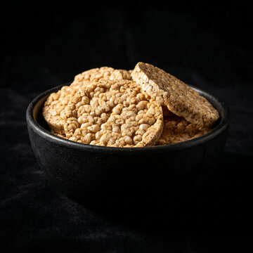 Bowl of crispy brown rice cakes on a dark textured background with breakfast nutrition alternative background minimalist wholesome vegetarian snacking ingredients crispbread