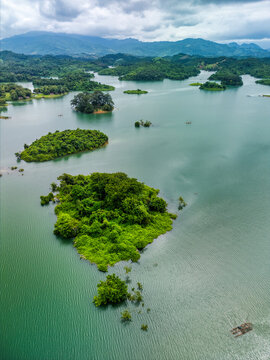 Aerial view of Nam Ngum Reservoir featuring lush green islands scattered across calm turquoise waters under a cloudy sky in Laos.