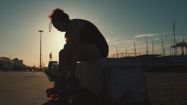 Silhouette of a woman tying her roller skates at sunset