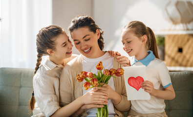 Fototapeta premium Happy Mother?s Day Celebration with Daughters Giving Flowers and Handmade Card at Home