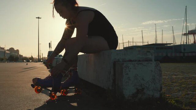 Tattooed woman tying roller skates at sunset