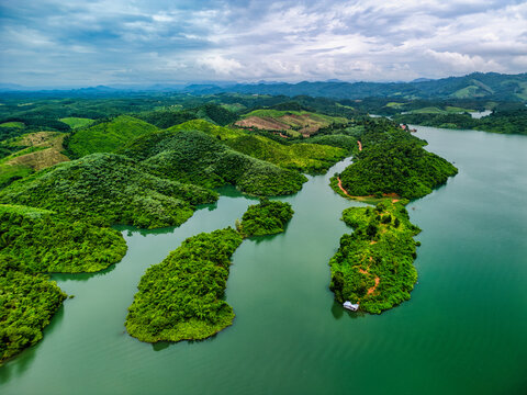 Aerial view of the Nam Ngum Reservoir with lush green islands and forested hills under a cloudy sky in Laos.