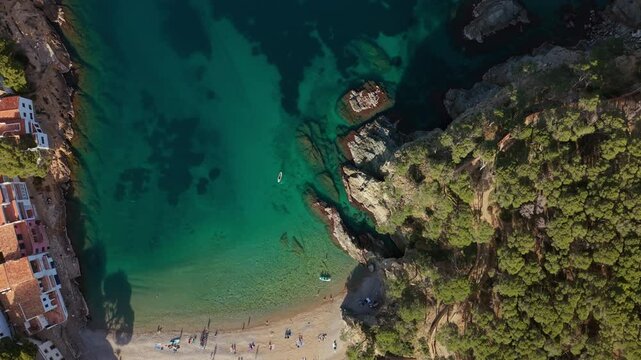 Top-down drone footage of the fishing village and cove of Cala sa Tuna, located in Begur, Catalonia. Showcases the charming beach, historic houses, and the surrounding Mediterranean landscape. 