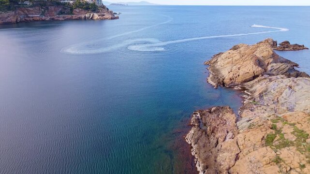 Aerial drone shot of a jet ski performing circular manoeuvres and creating wakes in the crystal clear turquoise waters of  Begur, Costa Brava, Spain. 