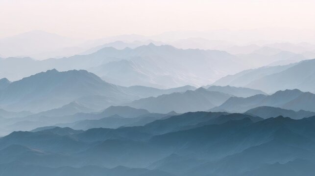 Landscape photograph of a mountain range. the mountains are covered in a layer of fog, giving them a hazy, misty appearance. the sky is a pale blue color, and the mountains are silhouetted against it.