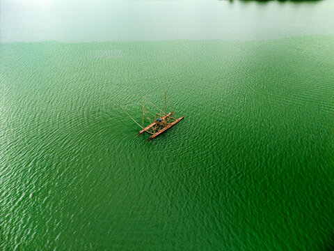 Aerial view of a traditional fishing boat with a large lift net on the green waters of Nam Ngum Reservoir, Laos.