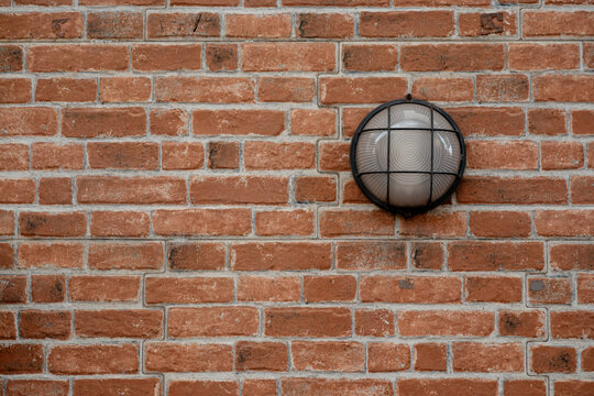 Red brick wall texture featuring a round industrial bulkhead light fixture. Ideal for architectural backgrounds and urban exterior design concepts.
