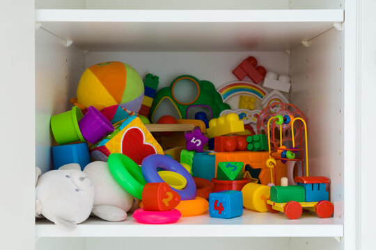 Different colorful messy baby playing toys on white wardrobe shelf at nursery room. Closeup. Front view.