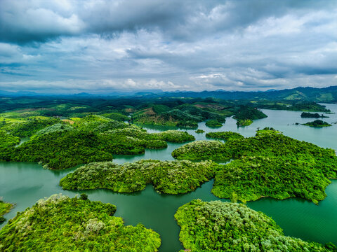 Aerial view of Nam Ngum Reservoir featuring lush green islands and dense tropical vegetation under a cloudy sky in Laos.