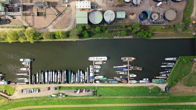 Aerial view of industrial chemical production factory on river bank with narrowboats docked and power station towers in the background and sunny rapeseed fields UK