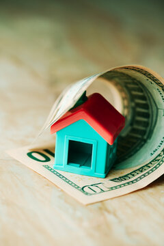 a small house emerging from a rolled dollar bill