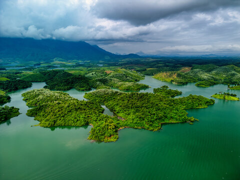 Aerial view of Nam Ngum Reservoir featuring lush green islands and distant mountains under a dramatic cloudy sky in Laos.