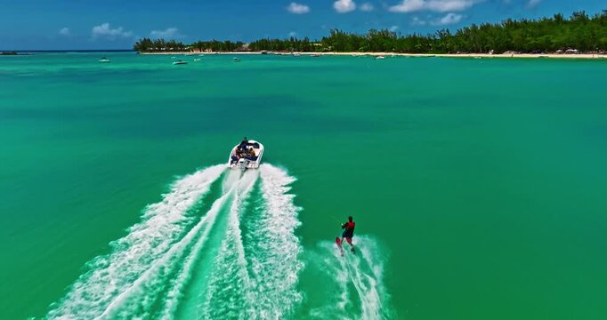 A drone view of a guy skiing behind a speedboat on crystal-clear water. Extreme sports, recreational activities