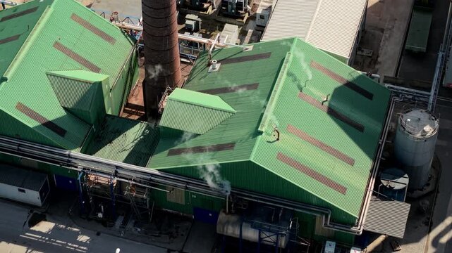 Close up aerial view of white steam venting from industrial building rooftop chimneys
