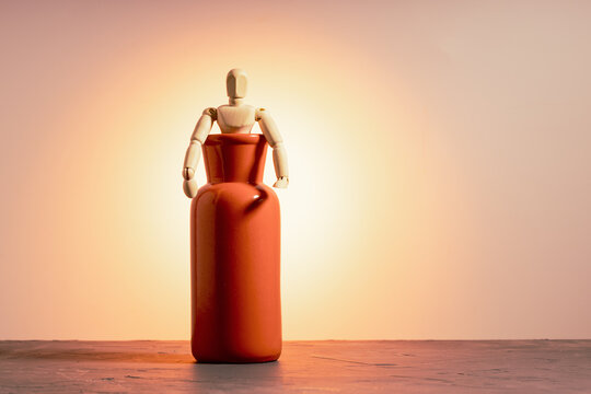 Wooden doll half emerging from red vase on orange background, escape and emergence concept