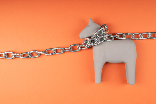 Miniature wooden horse chained on orange background, captivity and restraint symbolism