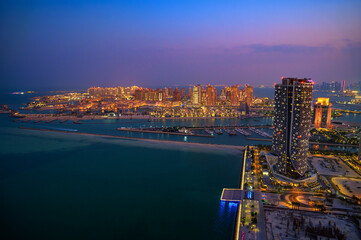 Obraz premium Aerial night view of Doha, Qatar, featuring illuminated skyscrapers, marina, and waterfront developments under a twilight sky along the Arabian Gulf
