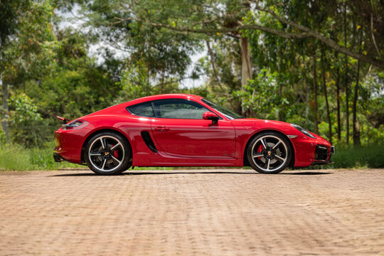 Red porsche cayman gts side profile in front of green forest, High performance luxury sportscar outdoors near nature