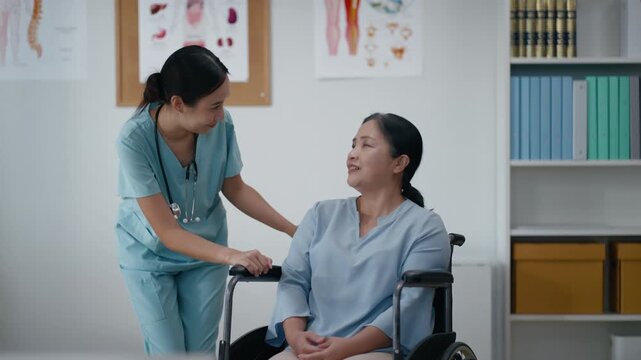 Asian nurse supporting senior woman patient in wheelchair during checkup at hospital or rehabilitation clinic.Smiling caregiver assisting elderly woman with friendly and supportive healthcare service
