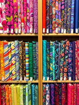 Multiple shelves are neatly stocked with vibrant fabric bolts, showcasing diverse colorful patterns and textures, creating an inviting display.