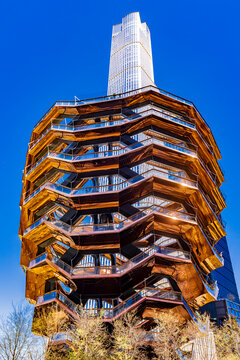 Following its official reopening in March 2026 with new safety features, Vessel stands as the centerpiece of the Hudson Yards Public Square, juxtaposed against the glass facade of 30 Hudson Yards.