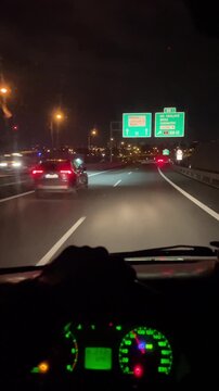 Hands on wheel night freeway exit signs, illuminated dashboard cluster, steady grip and focused driving, city lights approaching, vertical stock footage for transport scenes.