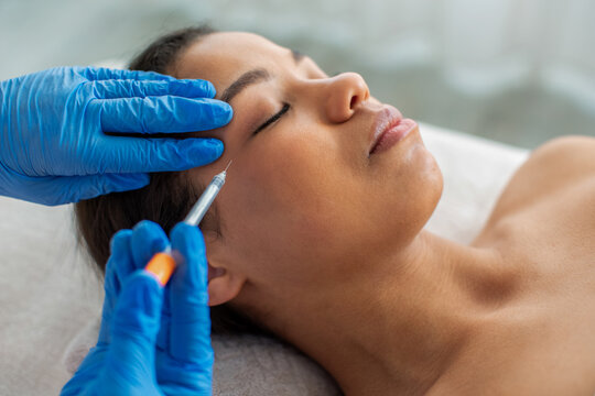 Young African American woman lying relaxed while receiving facial injection treatment at modern spa clinic, professional skincare and aesthetic procedure concept