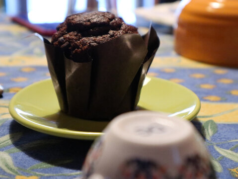 Muffin al cioccolato fondente servito su un piattino giallo, dettaglio di un dolce soffice in pirottino di carta scura su tavola colorata per colazione o merenda