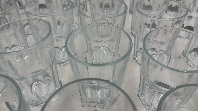 Rows of empty clear glass cups on white surface with reflections, useful as a transparent background