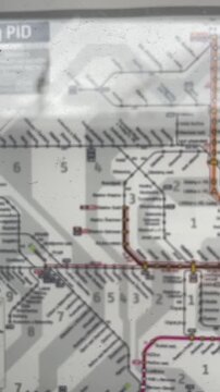 Vertical map closeup showing prague metro, folded paper map with colored transit lines, station names, zone numbers, blurred edges, soft indoor light, slow vertical pan