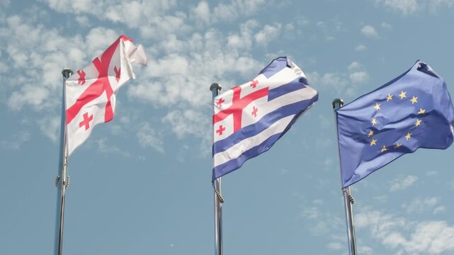 Flags of Europe, Georgia and Autonomous Republic of Adjara flutter against background clear blue sky with clouds