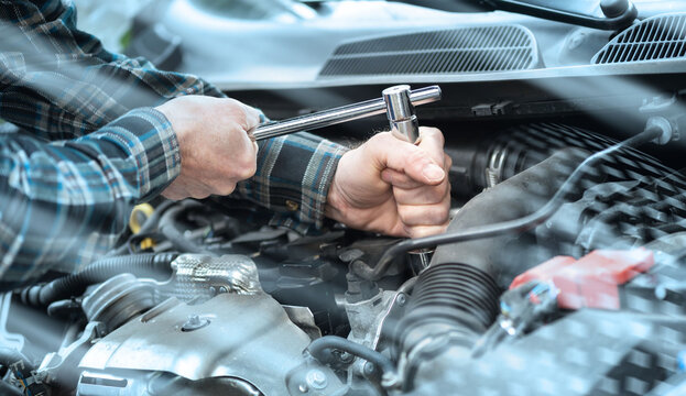 Hands of car mechanic working on car engine; light effect